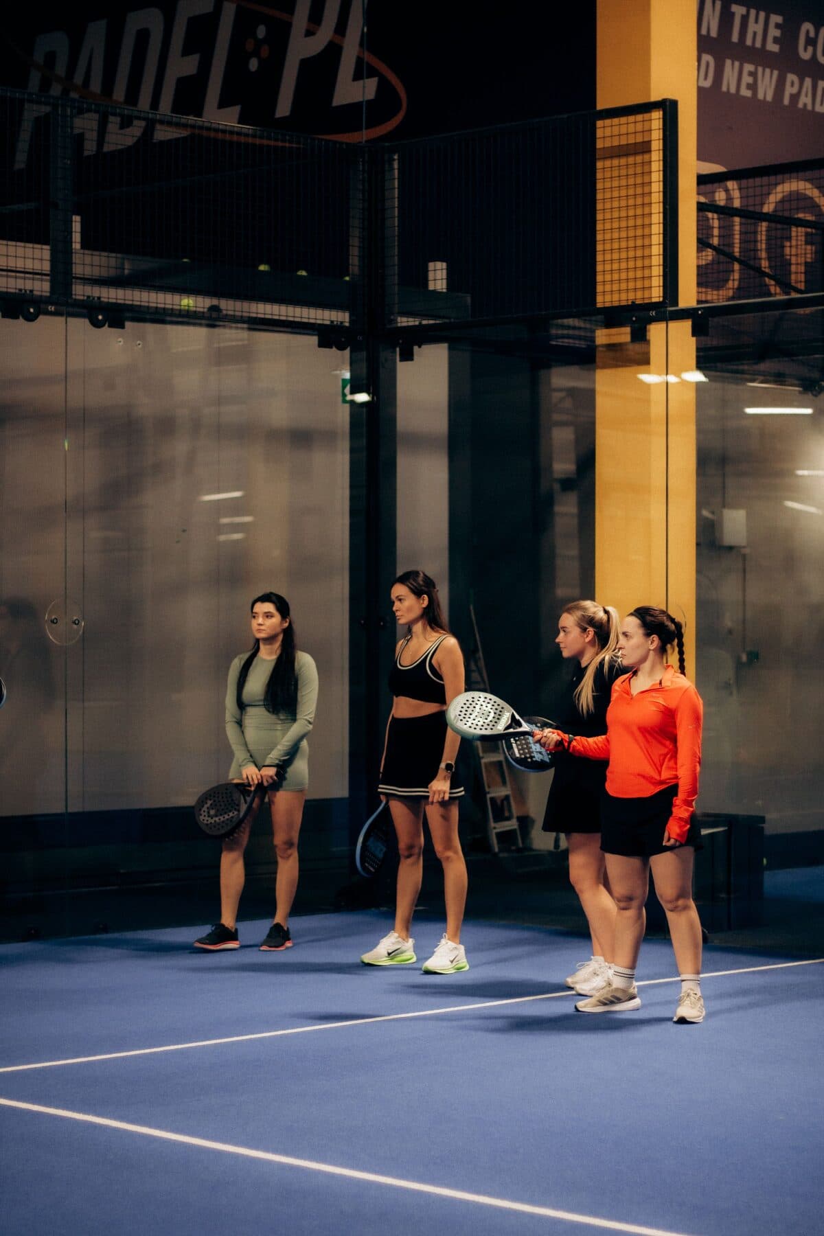 Jugadoras con raquetas en una cancha de pádel cubierta.