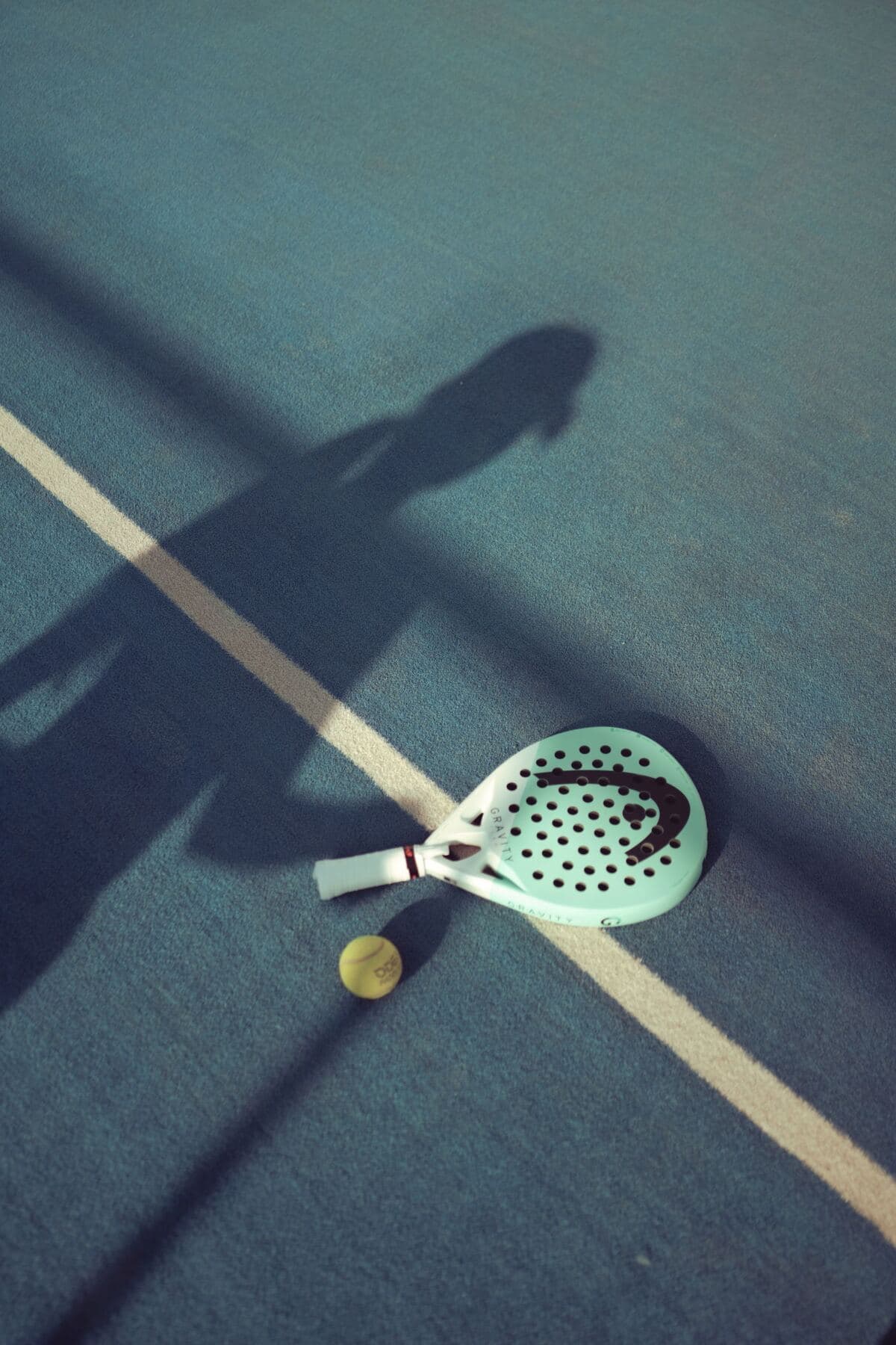 La sombra de una raqueta de pádel sobre el piso de la cancha.